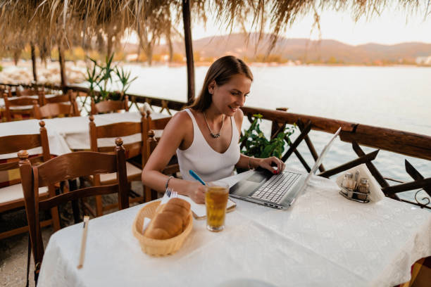 istock Young woman using a laptop in a restaurant at the seaside 1415313323