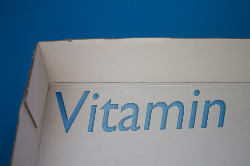 Vitamin word with cardboard box. Brown folded cardbox.