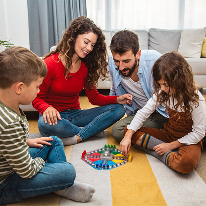 Young parents playing ludo game with their kids and having fun at home.