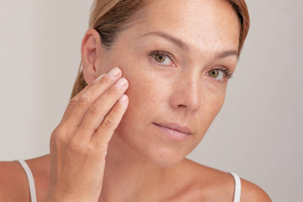 Woman with freckles on face touching skin Portrait of cropped caucasian middle aged woman face with freckles touching skin by hand on white background animal head stock pictures, royalty-free photos & images