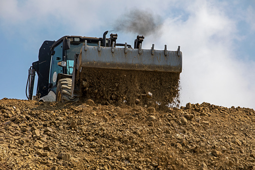 tractor with a large bucket of soil levels the road on a sunny hot day against the sky. Global construction.