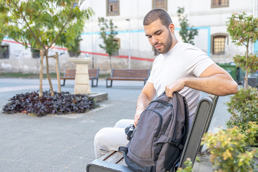 Man taking care of his backpack when resting on a park bench