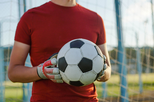 Portrait of young man football player goalkeeper wearing gloves holding soccer ball.