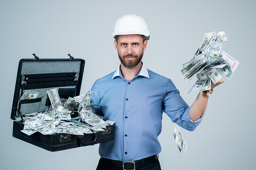 cheerful mature man businessman in building hard hat hold money case with dollar cash, income.