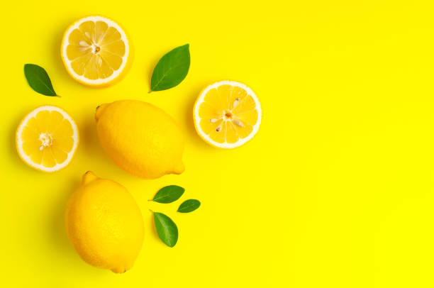 istock Creative background with fresh lemons and green leaves on bright yellow background. Top view flat lay copy space. Lemon fruit citrus minimal concept vitamin C. Composition with whole, slices of lemons 1415326928