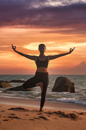 Woman yoga position arms raised on tropical sea coast or ocean beach outdoors at sunset. Female performing exercises for healthy lifestyle to restore strength and spirit. Yoga seashore. Copy space