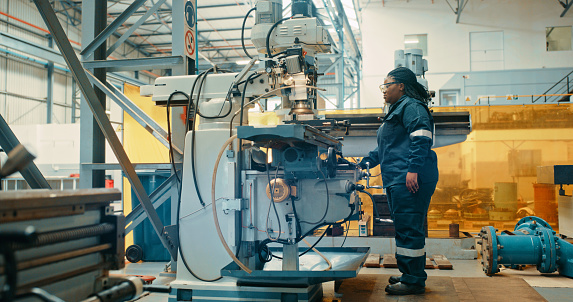 Engineer, mechanic or technician operating a lathe machine while working in a factory, workshop or factory. Female mechanical professional in coveralls shaping wood or metal in an industrial plant
