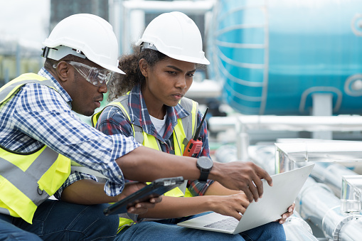 Group of African American engineer working in sewer pipes area at construction site. Male engineer and woman engineer discussing for maintenance sewer pipes, water tank on rooftop of building