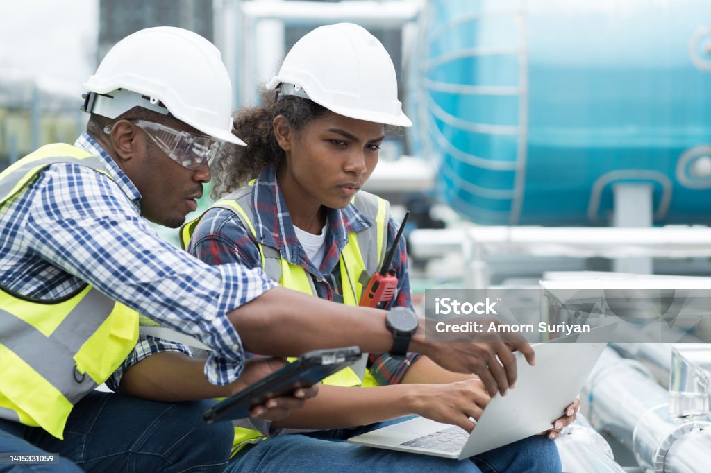 Group of African American engineer working in sewer pipes area at construction site. Male engineer and woman engineer discussing for maintenance sewer pipes, water tank on rooftop of building Trainee Stock Photo