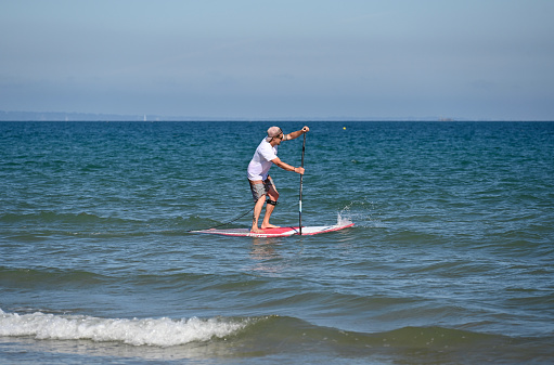 Erquy, France, July, 8, 2022 - Young man stand up paddling at Atlantic beach of Erquy, Brittany