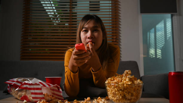 istock Young lady with remote control enjoying interesting movie and eating popcorn on sofa at night. 1415334162