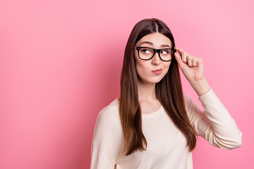 Portrait of attractive suspicious girl touching specs looking copy space solution isolated over pink pastel color background.