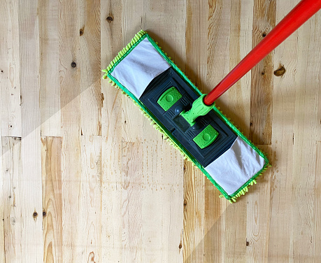 Cleaning wooden floor with green mop in house or office, laminate floor top view.