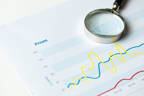 Price chart on printed paper with a magnifying glass on white background.