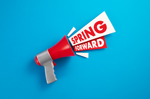 Red megaphone with colored papers and spring forward text on blue background