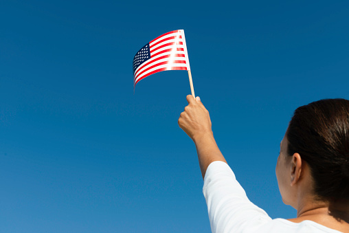 Back view of female who is waving American flag with clear blue sky in background.