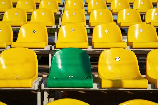 One green chair among yellow plastic seats on stands of stadium in open. Concept of sport lifestyle.