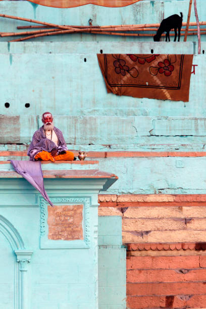 monje indio meditando en el techo del edificio y residente local lavable en el río ganges, filmado en la ciudad de varansi india en noviembre de 2009 - caste system fotografías e imágenes de stock