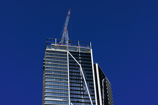 Tall office building nearing completion, with deep blue sky and a crane.