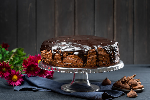Delicious Homemade Dark Chocolate Cake Dessert with Ganache glaze topping on the cake stand over dark rustic wooden background