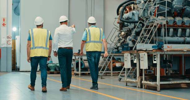 istock Professional mechanical engineers discussing upgrade plans on heavy production machines while walking in a warehouse. Expert machine specialist talking to colleagues about repairs and maintenance 1415349643