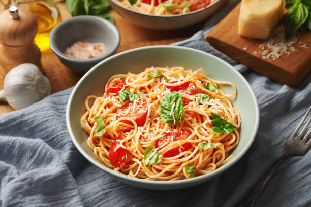 istock Plate of cooked spaghetti with cherry tomatoes and ingredients on the table 1415352904