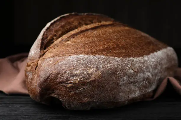 Loaf of tasty rye sodawater bread on black wooden table, closeup