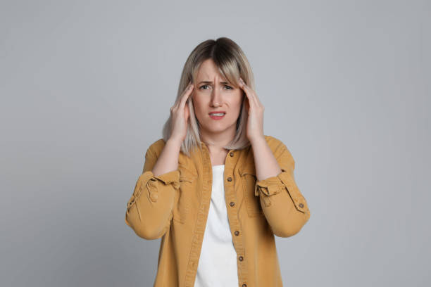 istock Woman suffering from headache on light grey background 1415354782