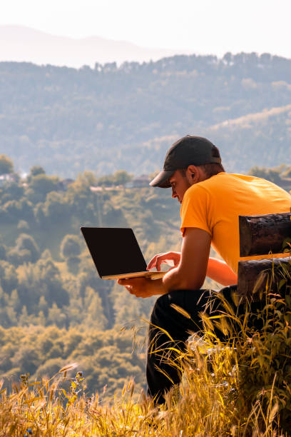 istock Young male traveler freelancer working, learning online outdoor, use laptop computer, notebook in nature against background of autumn mountain forest 1415354795
