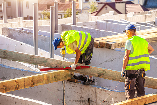 Builders working on roof of house. The roofer screws the roof crimp