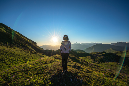 Silhouette of woman traveler standing alone against bright sunset sun in the mountains