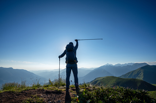 Hiker on top of the mountain raised arm with a hiking pole at sunset