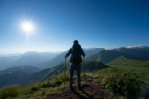 Hiker stands alone on top of the mountain at sunset, rear view