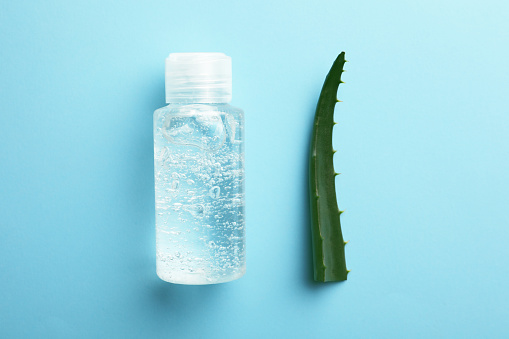 Bottle of cosmetic gel and aloe on light blue background, flat lay