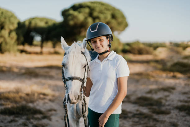 ritratto di ragazza di 12 anni in piedi con il casco in posa accanto al suo pony bianco - horse child pony little girls foto e immagini stock