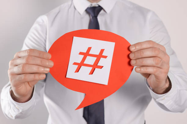 istock Man holding paper speech bubble with hashtag symbol on light background, closeup 1415358361