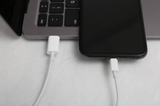 istock Smartphone connected with charge cable to laptop on light table, closeup 1415359076