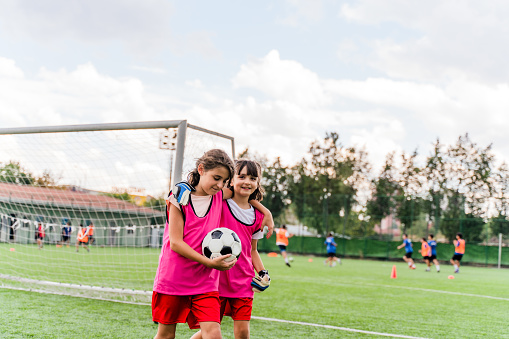 Two Happy Smiling girls in Sports Team Walking on Grass Pitch. Kids Making Sports Activity Outdoor.