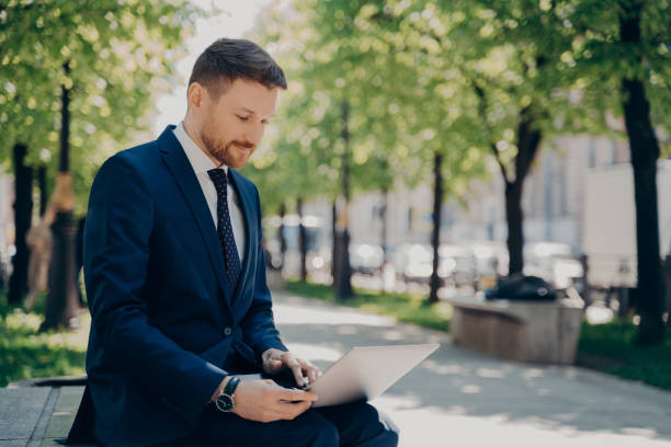 istock Young businessman working on laptop while sitting on bench in city park 1415359918