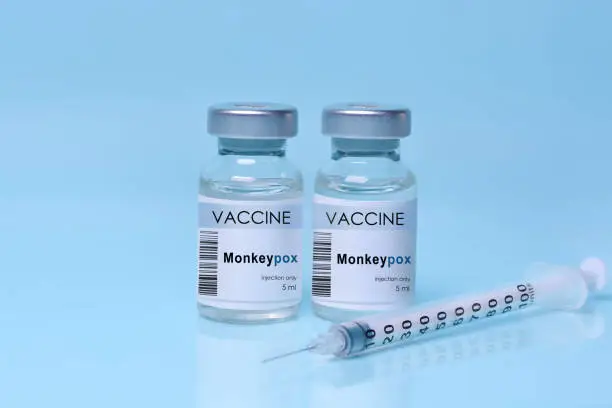 Photo of Two vials with vaccine Monkeypox with a syringe on a blue background.The concept of medicine, healthcare. Monkeypox is a viral zoonotic disease. Monkeys may harbor the virus and infect people.