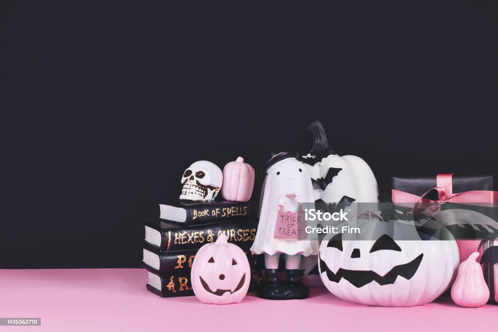 Pink and white Halloween decor Pink and white Halloween decor with black and white pumpkins, spell books and spiders on black background  with copy space Halloween Stock Photo