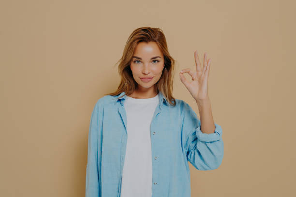 istock Young lady expressing approval with okay gesture on beige background 1415364020