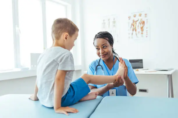 Photo of Female orthopedist examining little child foot condition in clinic