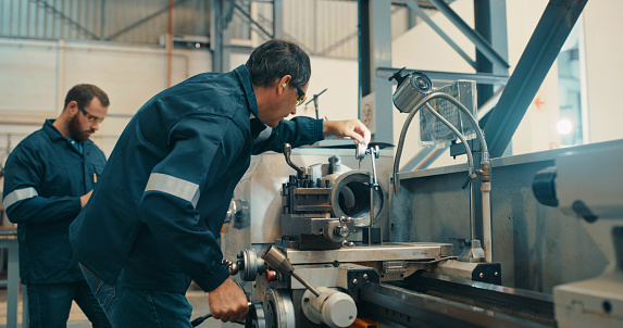 Professional mechanical engineers working on a heavy metal machine in a workshop or warehouse. Expert repairman collaborating as a team to upgrade parts and maintenance in a steel production factory