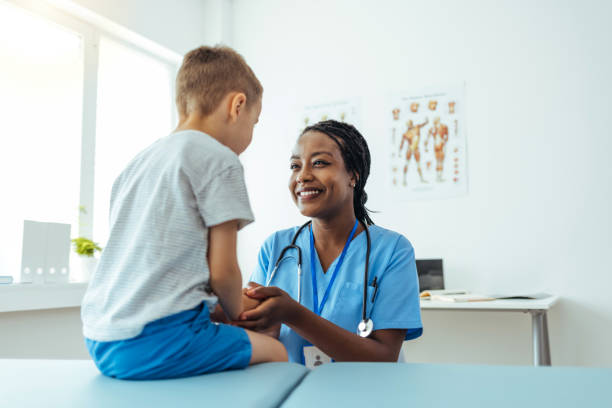 medico donna che consola il suo giovane paziente e gli tiene la mano - nurse doctor healthcare and medicine african descent foto e immagini stock