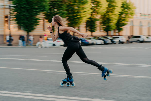Professional female roller demonstrates her abilities of rollerblading rides very quckly on road along city enjoys sunny day dressed in black active wear. Active lifestyle hobby and fitness activity