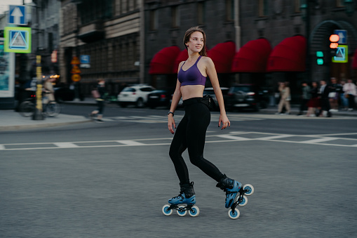 Full length shot of active slim young woman dressed in sportsclothes rides on rollers to strengthen arms and legs muscles improves balance agility and coordination has good mood burns calories