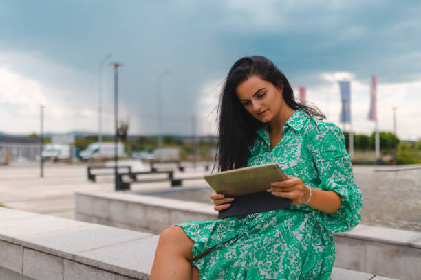 istock Young woman in a sundress using a tablet in an urban downtown environment 1415366179