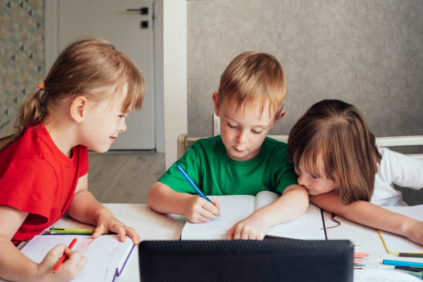 istock Children sit at a table with pens and notebooks and use a laptop 1415367521