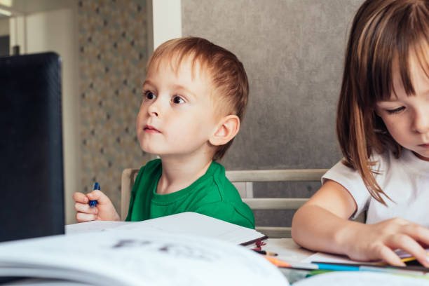 istock Boy sits at the table, uses a laptop and writes in a notebook 1415367523